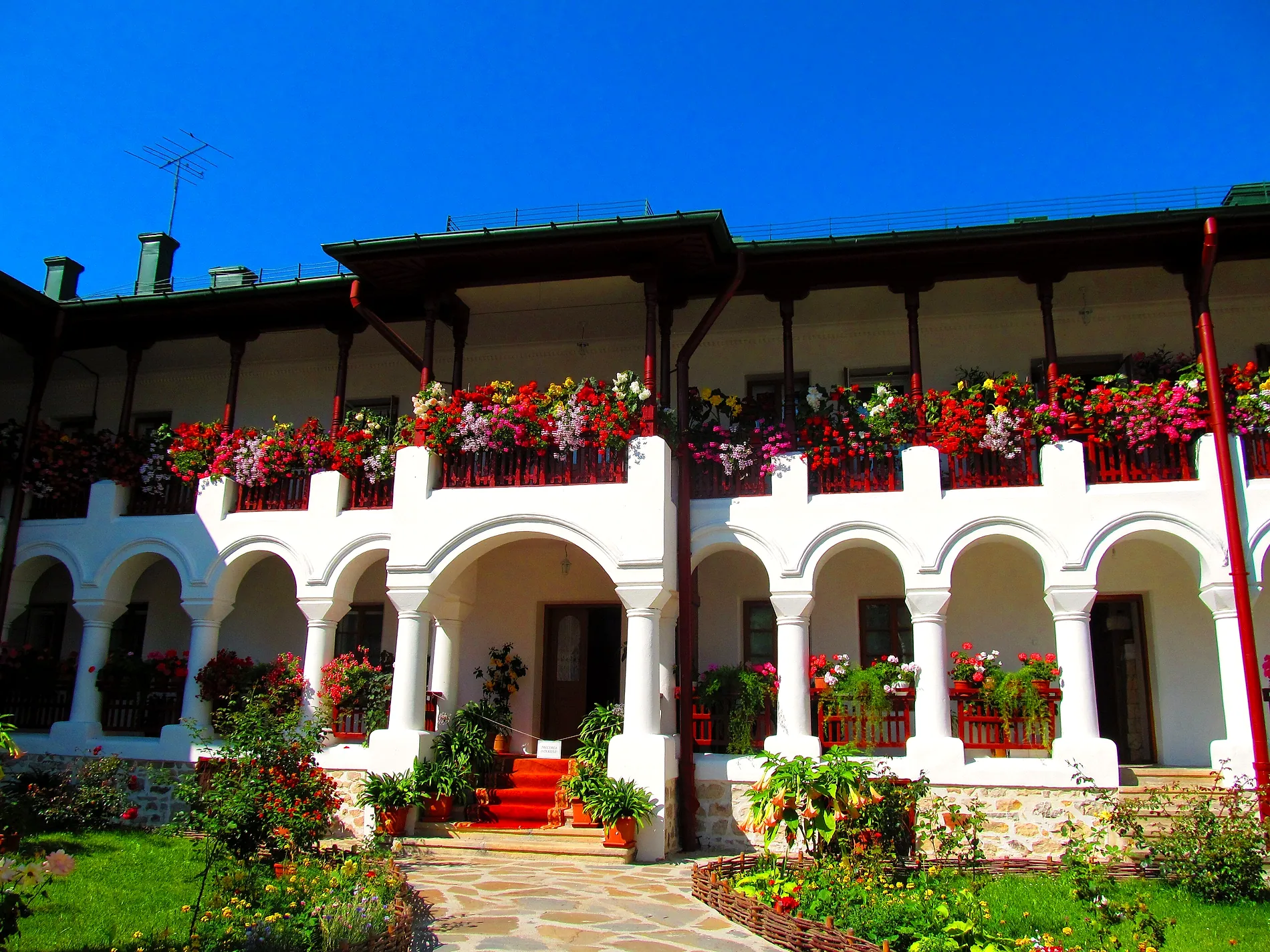 The arcaded gallery of the monastery buildings, full of flowers under a blue sky