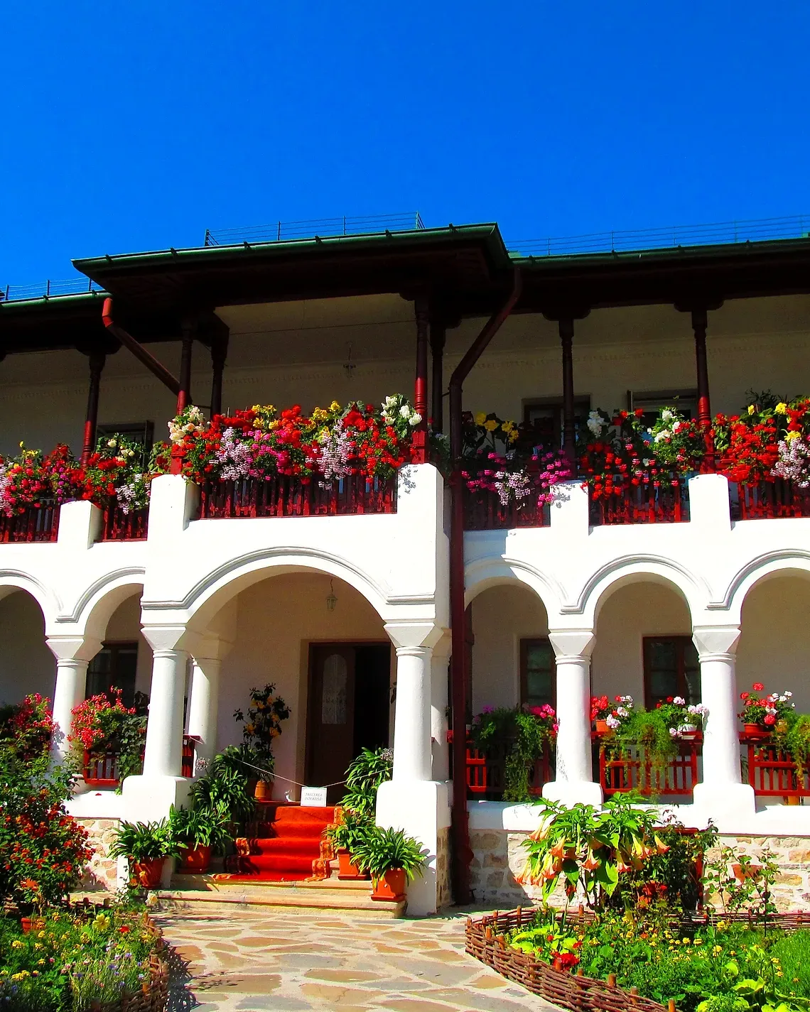 The arcaded gallery of the monastery buildings, full of flowers under a blue sky
